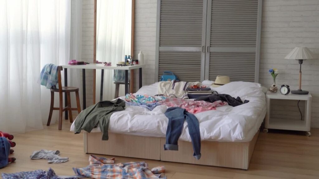 Dormitorio con ropa desordenada sobre la cama y el suelo.
